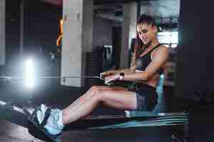 Free photo young woman in sportswear in the gym, training and pulling weights in seated cable row machine.