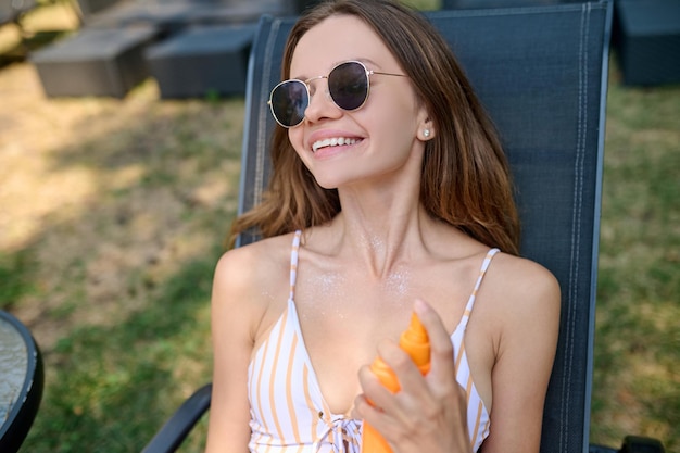 Young woman spraying spf cream on her body