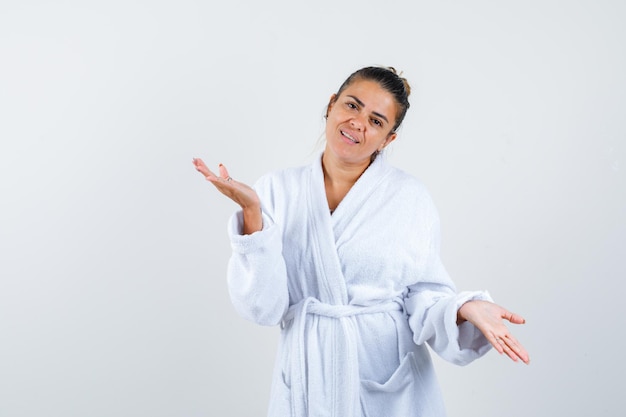 Young woman spreading palms aside in bathrobe and looking happy