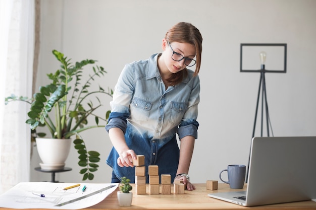 Free photo young woman stacking wooden block on work desk at office