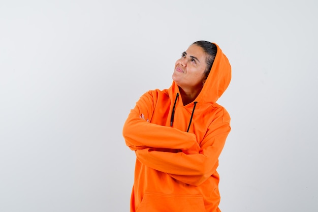 Young woman standing arms crossed, looking away in orange hoodie and looking radiant 