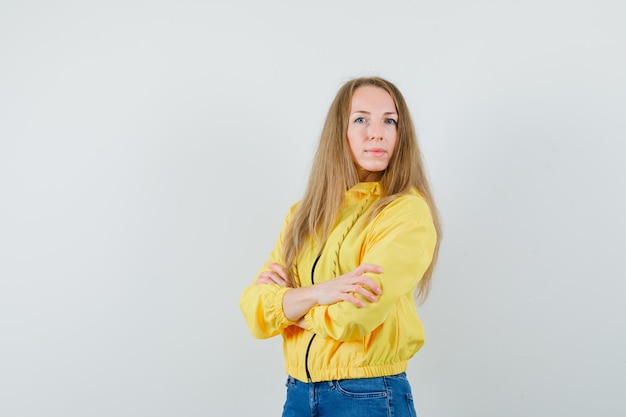 Young woman standing arms crossed in yellow bomber jacket and blue jean and looking elegant , front view.