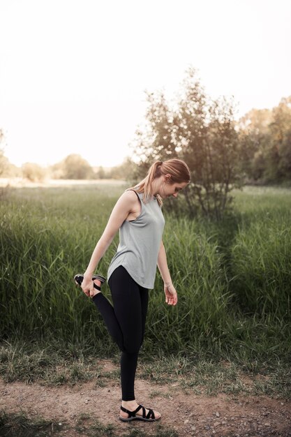 Young woman standing in field stretching her leg