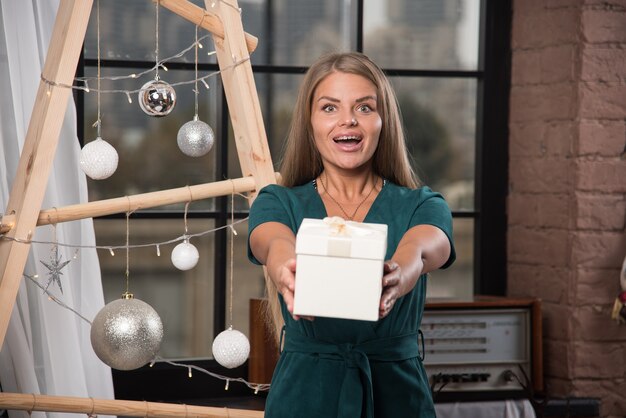 Free photo a young woman standing and giving a christmas present near christmas balls