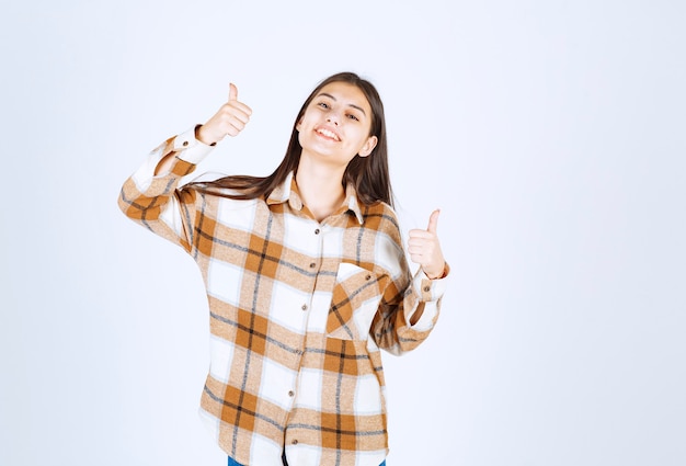 young woman standing and giving thumb up on white wall. 