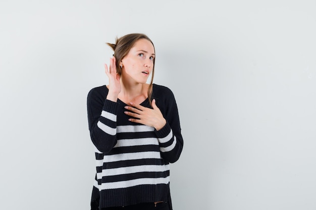 Young woman standing in listening pose in striped knitwear and black pants and looking focused