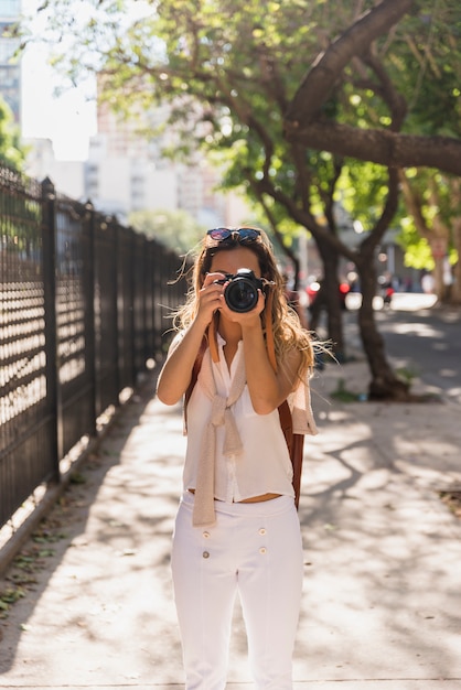 Free Photo young woman standing in the park taking photo from camera