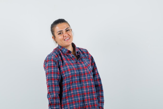 Young woman standing straight and posing at camera in checked shirt and looking pretty , front view.