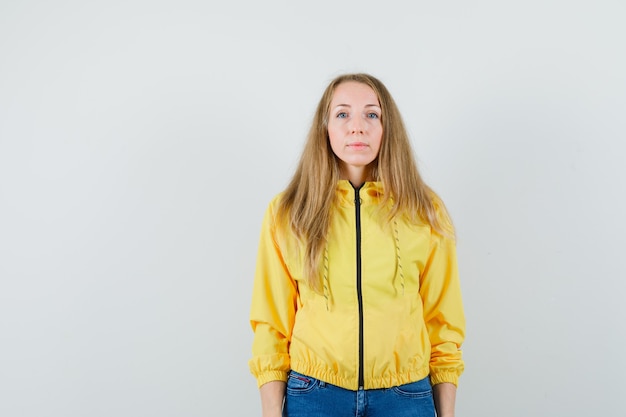 Free Photo young woman standing straight and posing at the camera in yellow bomber jacket and blue jean and looking optimistic , front view.