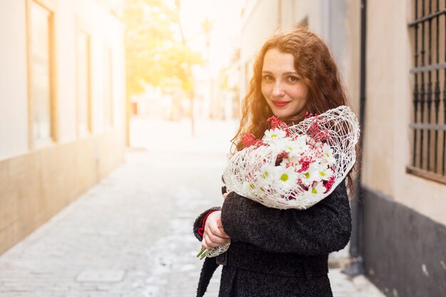 Free photo young woman standing in street with flowers