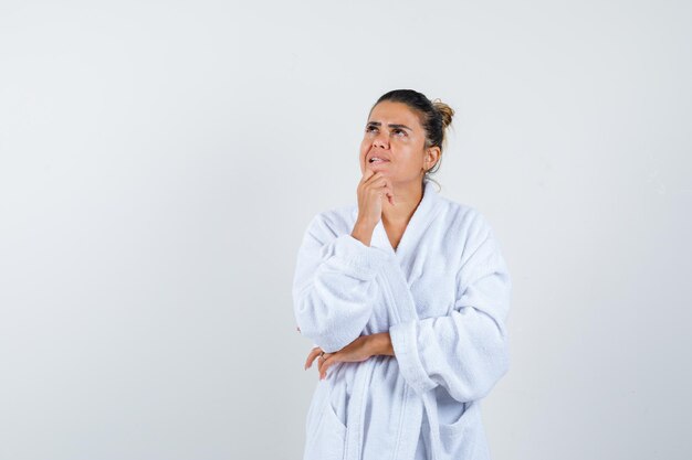 Young woman standing in thinking pose in bathrobe and looking pensive