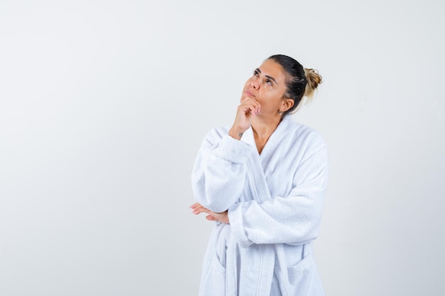 Young woman standing in thinking pose in bathrobe and looking thoughtful