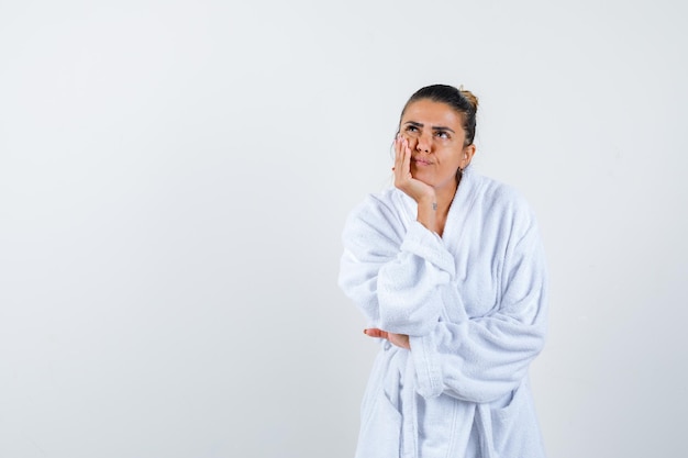 Young woman standing in thinking pose in bathrobe and looking thoughtful