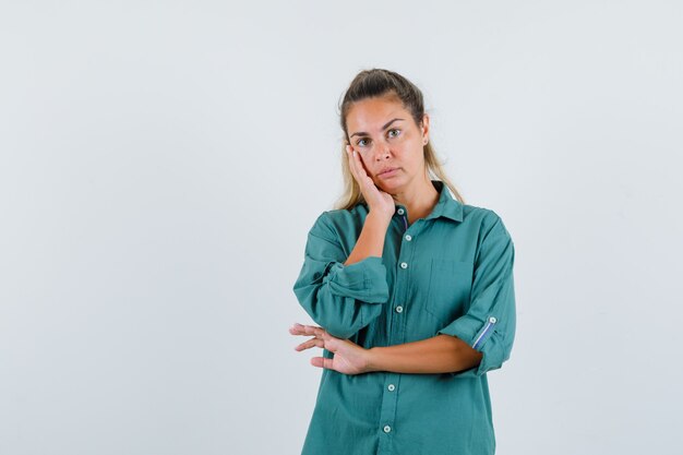 Young woman standing in thinking pose in green blouse and looking pensive