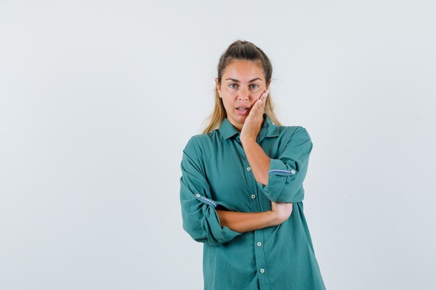 Young woman standing in thinking pose in green blouse and looking pensive