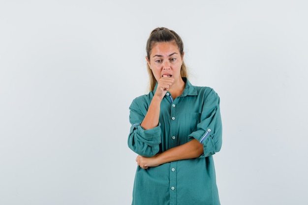 Young woman standing in thinking pose in green blouse and looking pensive