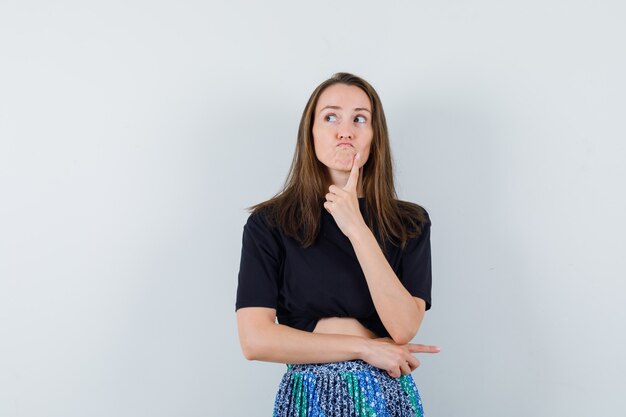 Young woman standing in thinking pose and looking away in black t-shirt and blue skirt and looking pensive