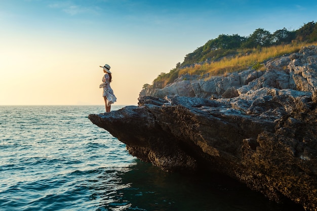 Free photo young woman standing on the top of rock and looking at the seashore and sunset in si chang island.