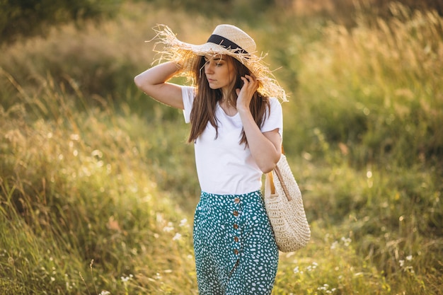 Young woman standing with bag in big hat in field