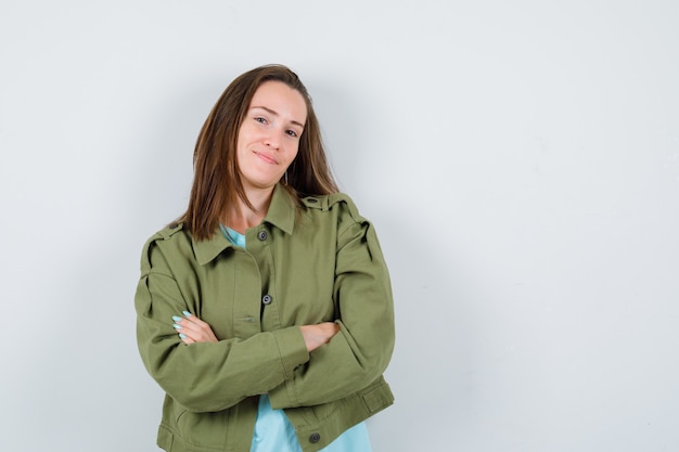 Young woman standing with crossed arms in green jacket and looking confident , front view.