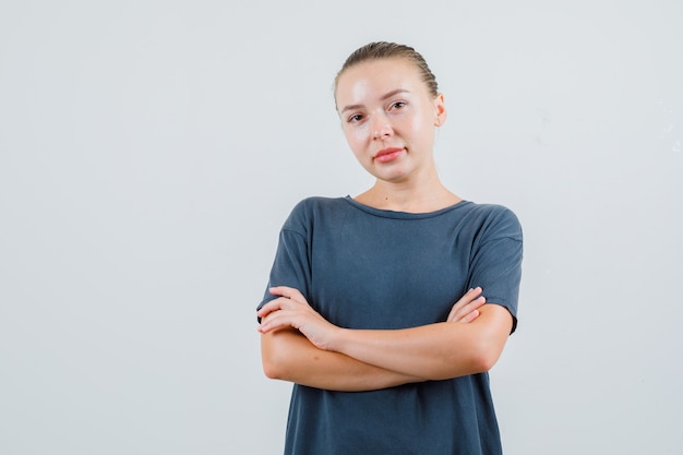 Young woman standing with crossed arms in grey t-shirt and looking confident