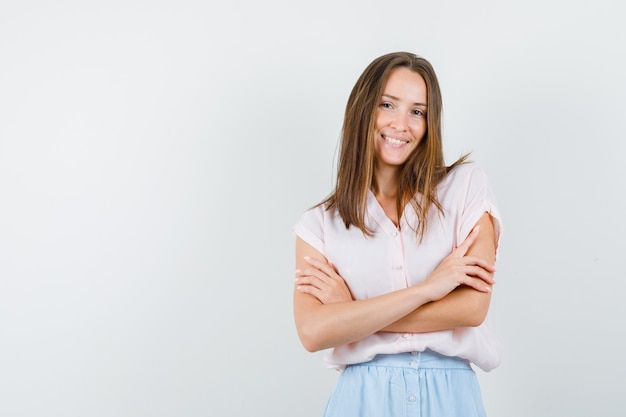 Young woman standing with crossed arms in t-shirt, skirt and looking cheerful. front view.