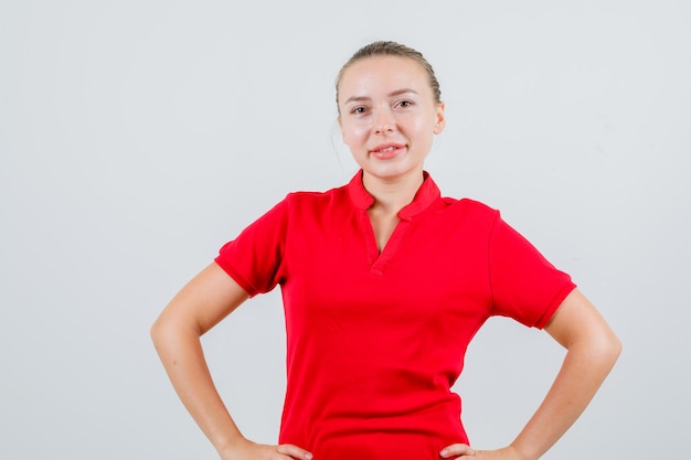 Young woman standing with hands on waist in red t-shirt and looking confident