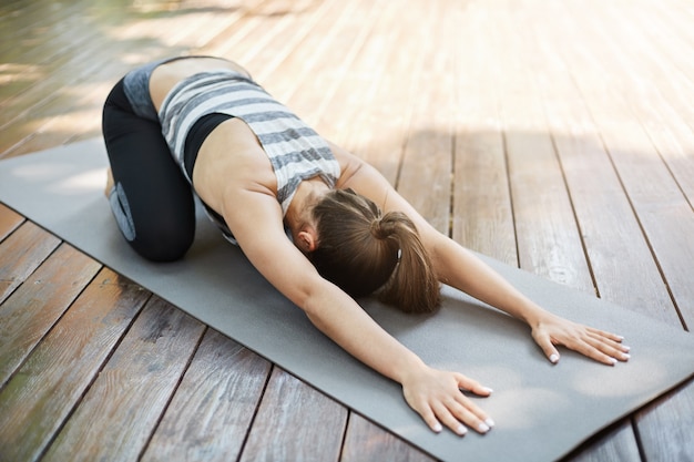 Free photo young woman stretching her back after a long yoga session. doing exercises in her backyard for neighbours to envy.