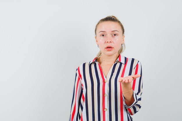 Young woman stretching her hand in questioning manner in striped blouse