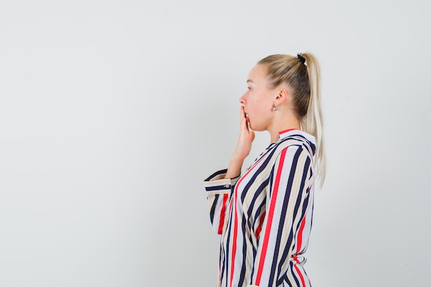 Young woman in striped blouse covering her mouth with one hand and looking shocked