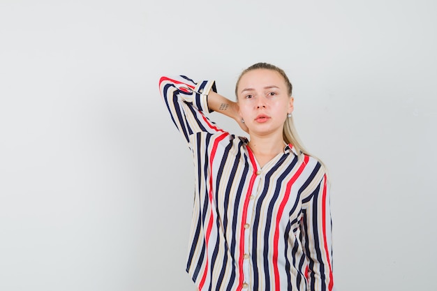 Free photo young woman in striped blouse putting her arm behind head and looking pretty