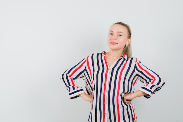 Free photo young woman in striped blouse putting her both hands on hips and looking happy