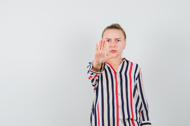 Young woman in striped blouse showing stop sign and looking angry