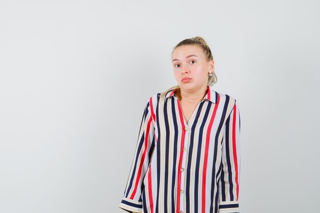 Young woman in striped blouse shrugging her shoulders and looking undecided