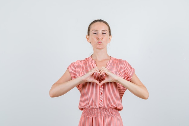 Young woman in striped dress making heart shape with hands , front view.