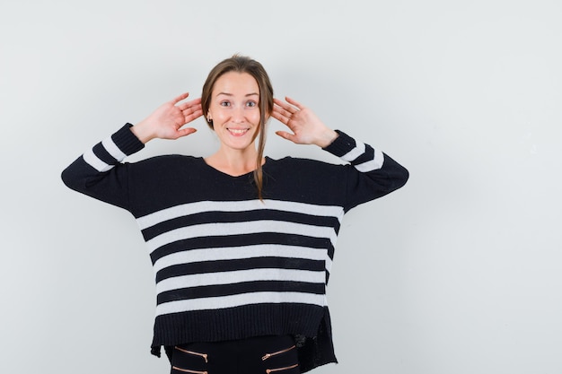 Free Photo young woman in striped knitwear and black pants holding hands near ear and looking happy