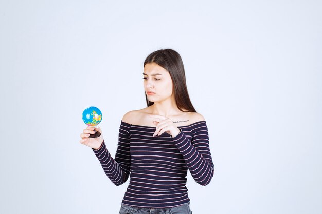 Young woman in striped shirt holding a mini globe and guessing a place over it