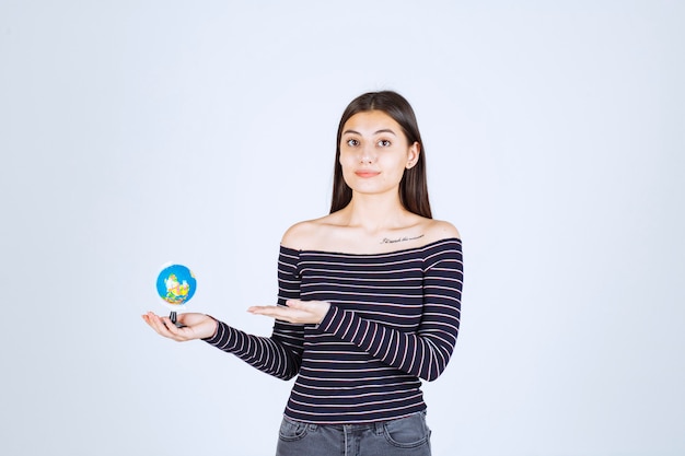 Young woman in striped shirt holding a mini globe and pointing at it