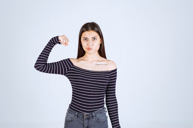 Young woman in striped shirt showing her arm muscle and fist