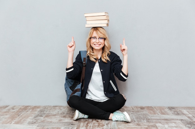 Free photo young woman student holding books on head and pointing