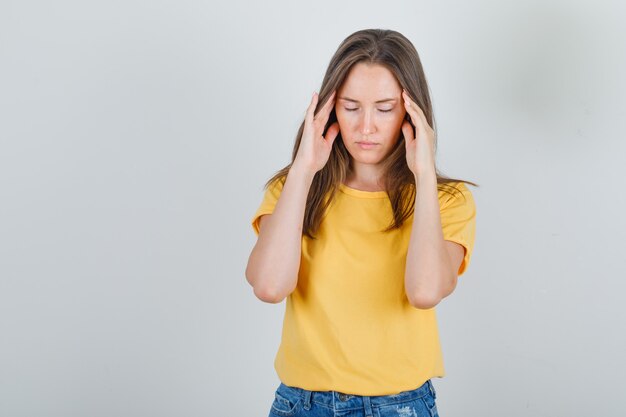 Young woman suffering from headache in t-shirt, shorts and looking tired