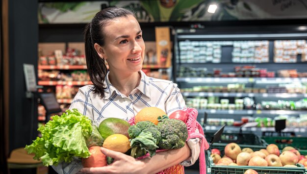 Young woman in a supermarket with vegetables and fruits buying groceries