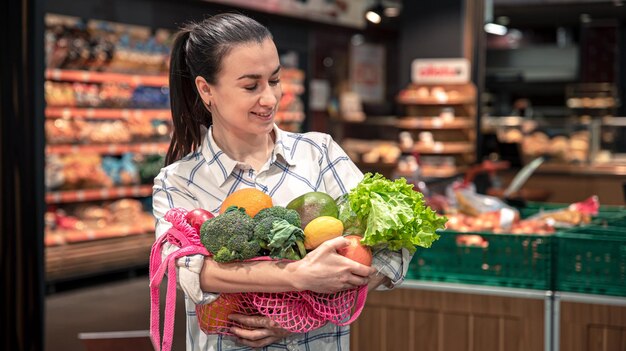 Young woman in a supermarket with vegetables and fruits buying groceries