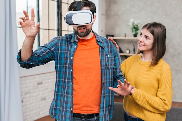 Free photo young woman supporting the man wearing virtual reality camera touching his hands in air