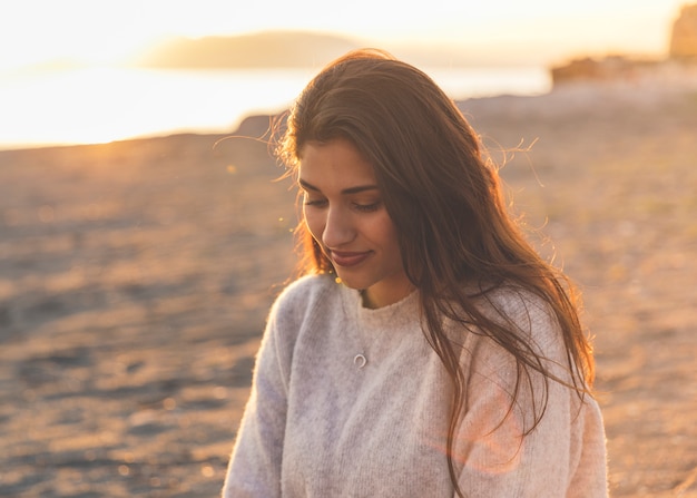 Free photo young woman in sweater sitting on sandy sea shore