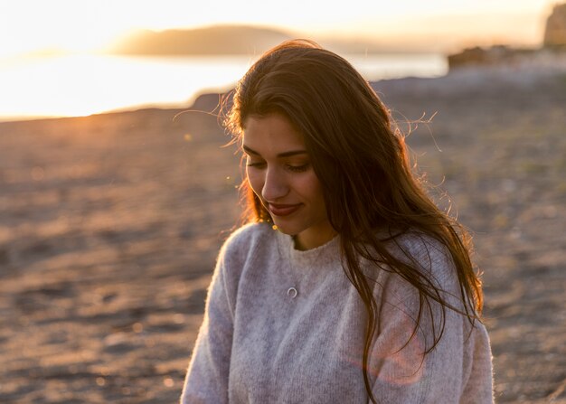 Young woman in sweater sitting on sea shore 