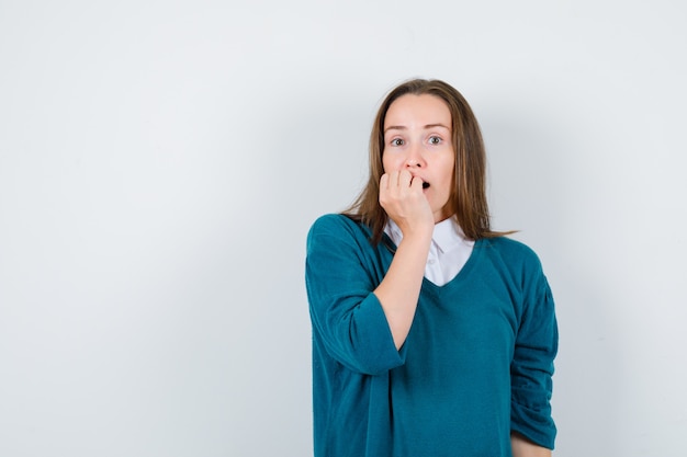 Young woman in sweater over white shirt biting nails and looking puzzled , front view.