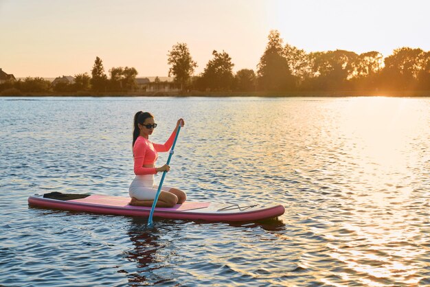 Young woman swimming on sup board during sunset