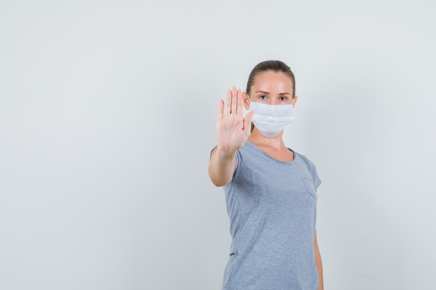 Young woman in t-shirt, mask showing refusal gesture and looking serious , front view.