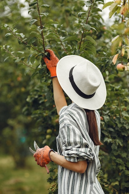 Free photo young woman taking care of plants. brunette in a hat and gloves. woman use aveeuncator.